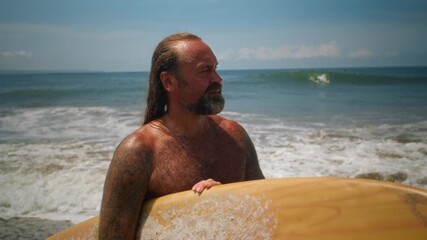 Happy fit senior having fun surfing at sunset time. Sporty bearded old man training with surfboard on the ocean beach. Elderly healthy male lifestyle, extreme sport concept. Active lifestyle, tropical - Powered by Adobe