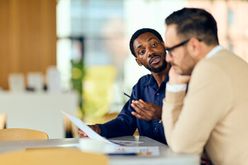 African Man Explains Document To Colleague During Casual Business Meeting In Modern Space