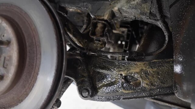 Handheld close-up looking past rear brake disc to suspension and chassis showing control arms, beams coated with lanolin rust protection product.