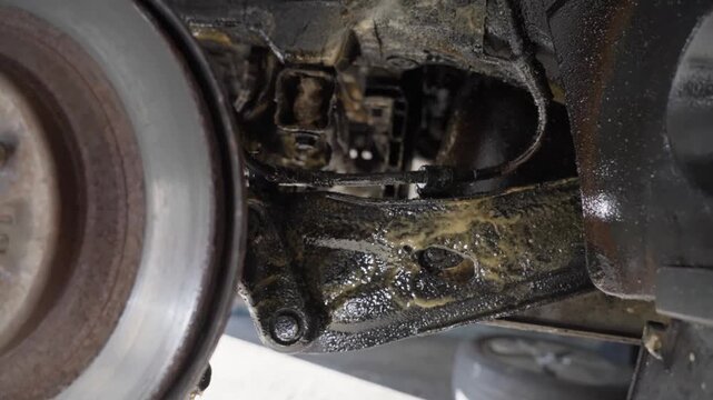 Slow, handheld push in past rear brake disc showing car suspension, control arms and beams coated with lanolin rust protection product.
