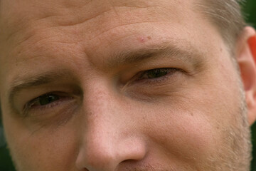 Human Man Face extreme close up. Macro Shot of Male Green Eye. Vision. Healthy Eyesight Concept. Front view. Mature Adult Looking at Camera, Blinking Eyelashes. Eye Opening Wide. Soft Selective Focus