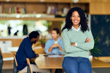 African-American Woman Smiles Confidently At A Modern Library Café While Friends Work Nearby