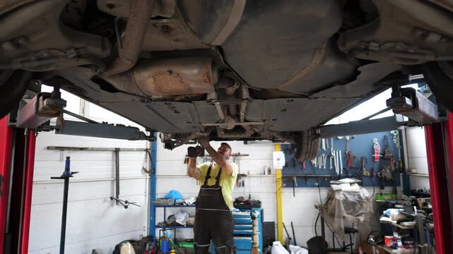 Mechanic performing detailed inspection and repair on vehicle undercarriage in auto service garage, showcasing tools, equipment, and focused craftsmanship in a professional environment