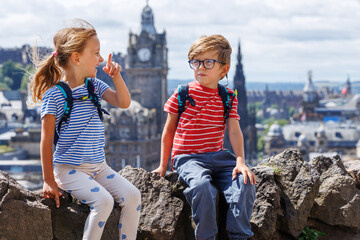 Two children with backpacks enjoy city views, smiling happily