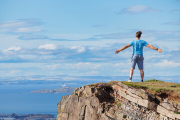 Person hiker stands triumphantly with open arms on a steep cliff