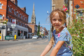 Girl smiles on a sunny street, flowers bloom nearby, Farnham, UK