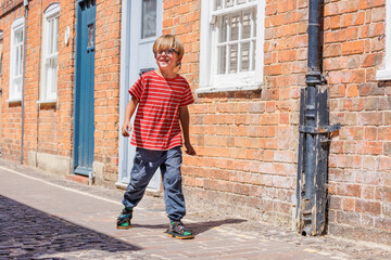 Boy in striped shirt walks joyfully along a sunny brick street