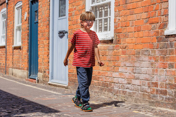 Little boy walks in sunny, brick-filled street at Farnham, UK