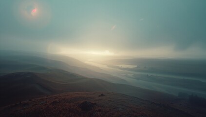 Obraz premium Morning mist covering winding river valley on hillside under low sun with grassy hills, lens flare