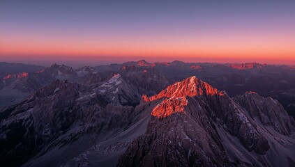 Naklejka premium Bathing jagged mountain peak in pink-red alpenglow at dawn, with snow patches and ridges