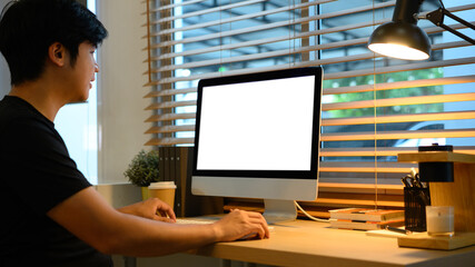 Man working on desktop computer in home office with coffee cup and warm light