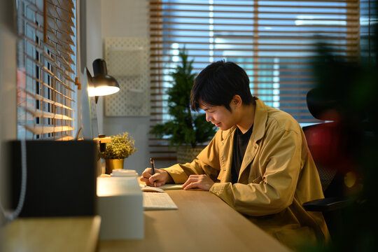 Freelancer writing notes at cozy home office desk with computer and warm light, concept creativity, planning