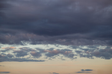 Dark dense clouds at sunset in the blue sky with reflections of the evening sun and breaking dark clouds in the sunset haze.