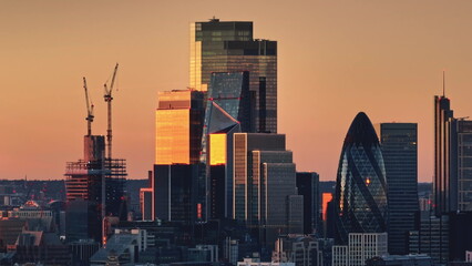 Bright orange sunset light over modern glass skyscrapers in London's financial district, iconic...