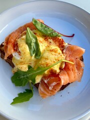 Close-up of a delicious gourmet toast topped with smoked salmon, poached egg, and creamy hollandaise sauce, garnished with fresh arugula leaves and paprika. Elegant restaurant-style breakfas