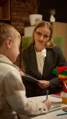 Psychologist smiling at boy drawing with colored pencils during therapy with toy blocks. Concept of...