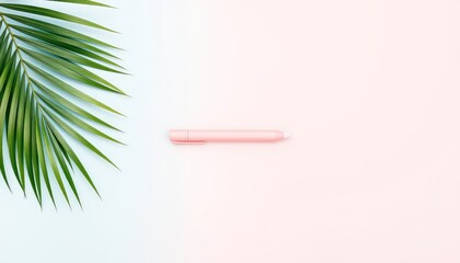 Green palm leaf and pink stylus pen on pastel pink and blue background creating a simple graphic composition
