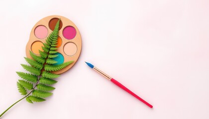 Artistic concept of paint palette, brush, and a fern leaf on a light colored backdrop