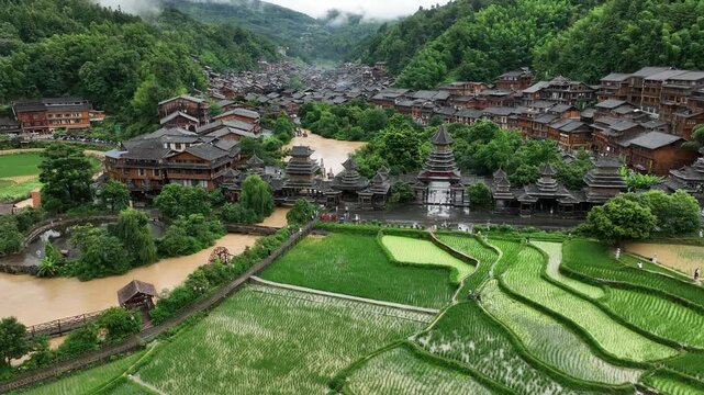 Aerial view of the traditional wooden houses nestled amidst lush green hills with a river flowing through Zhaoxing Dong Village, Guizhou, China.