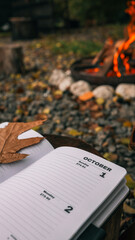 October 1st in a journal with a fall leaf and a cozy campfire in the background