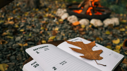 Autumn scene with a calendar, a leaf, and a warm campfire in the background