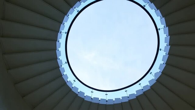 Upward view of a contemporary spiral staircase with circular skylight