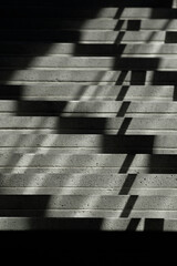 Concrete staircase lit by natural sunlight casting angular shadows through a railing. The image...