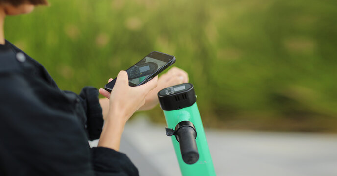 Cropped photo of woman with smartphone scans QR code for electric scooter rental. Girl using app on phone to unlock dockless transport outdoors. Urban riding ecological vehicle. Modern technology
