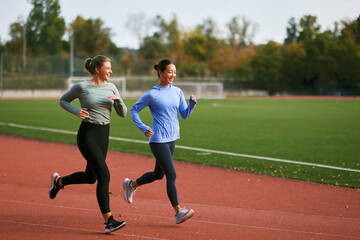 Two diverse women jogging together on a stadium track, exercising for a healthy lifestyle