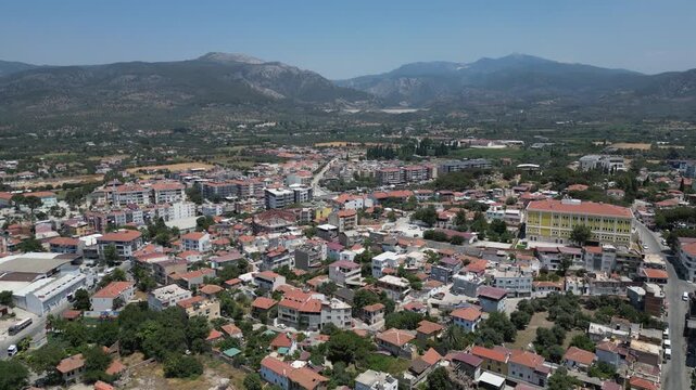 Aerial view of buildings with red rooftops contrasting with a yellow building and mountains in the background, Milas, Mugla, Turkey.