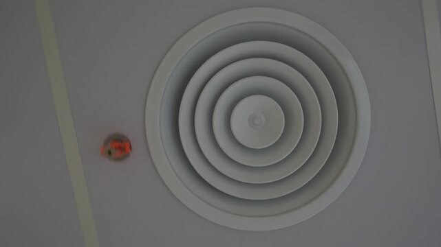 Bottom view of a modern suspended ceiling in a new apartment with a circular ventilation grille and fire sprinkler system. The camera moves creating a rotation effect that highlights ceiling details.