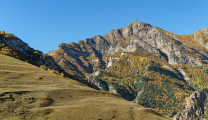 Majestic mountain peaks with rugged cliffs and autumn foliage under  clear blue sky, showcasing the beauty of wild, untouched landscape. Kabardino-Balkaria. El-Tyubu