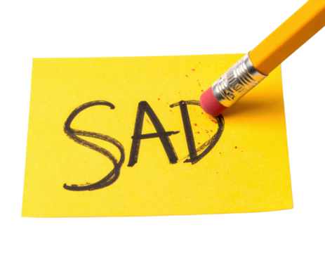 A pencil eraser is partially erasing the word "SAD" written on a yellow sticky note, symbolizing the emotions we try to overcome.