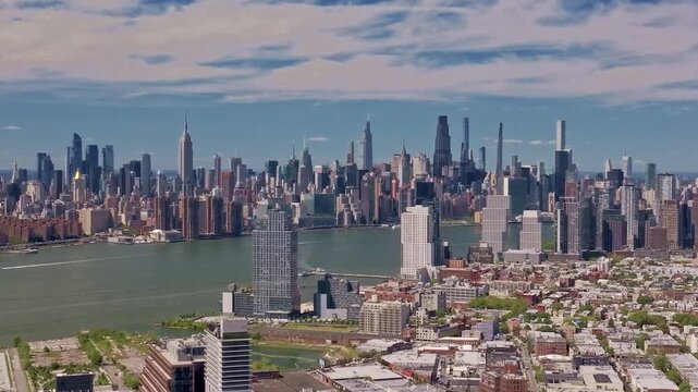 This cinematic drone footage captures the iconic New York City skyline as seen from Brooklyn across the East River, a breathtaking scenery of towering skyscrapers, including the Empire State Building.