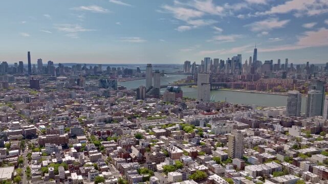 A cinematic aerial drone shot captured from the Brooklyn side, featuring the Williamsburg bridge crossing the East river into lower Manhattan, with the iconic Freedom tower, of New York City.