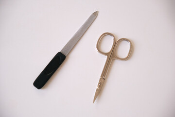 Close-up of a metal nail file and small manicure scissors placed on a clean white surface, minimal composition emphasizing grooming tools, personal care, and tidy beauty routine.