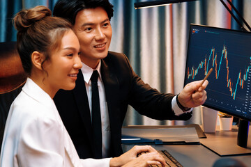 Smiling Asian business traders pointing to dynamic stock exchange data screen profit value online...