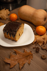 A glazed pumpkin cake with chocolate on a plate. Autumn decor, tangerines, and squash enhance the festive atmosphere.