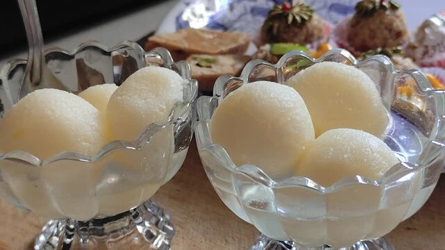 Indian sweet spongy Rasgulla taking from a transparent glass bowl filled with sugar syrup. Bengali mithai Rasgulla.