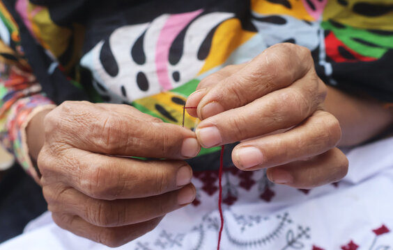 A skilled artisan carefully inserting threading into a needle to complete a beautiful floral design. Every stitch shows precision, dedication, and the art of creating something truly unique