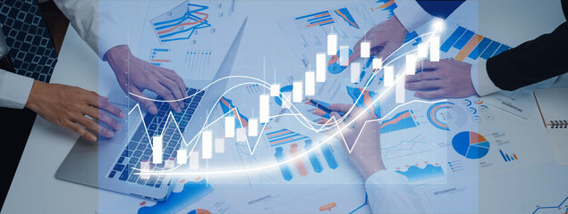 A diverse group of professionals collaborates over financial data and statistics using laptops and graphs for strategic planning in a modern office environment. Axiom