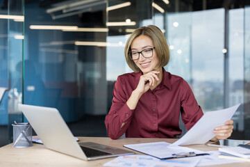 Young asian businesswoman in glasses smiling happily while reviewing documents and working with a...