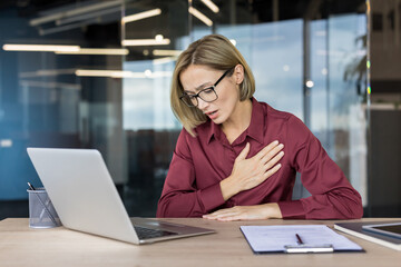 Businesswoman experiencing sudden chest pain and shortness of breath while working on her laptop in...