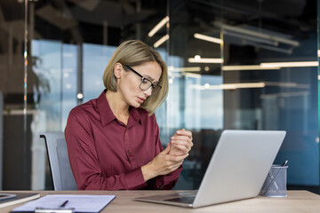 Businesswoman experiencing wrist discomfort and carpal tunnel symptoms while typing on laptop,...