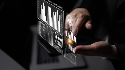 Businessman engages with a holographic interface to analyze marketing planning through interactive charts and data visualization, showcasing modern technology in a corporate setting. Impute