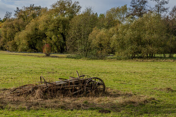 Alte Holzfarmger&auml;te liegen in einer Wiese, umgeben von B&auml;umen im Herbstlicht
