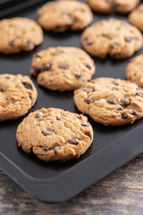 Baked chocolate chip cookies on a black baking tray