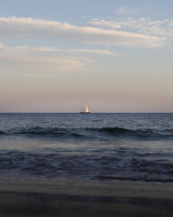 Fototapeta premium Sailboat on the horizon at sunset over calm sea