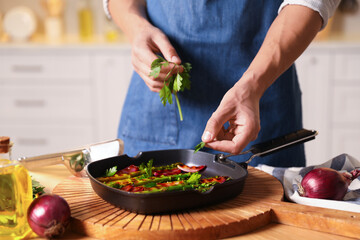 Man adding parsley into pan with grilled vegetables at table indoors, closeup
