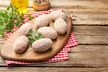 Uncooked meat patties, parsley, peppercorns and oil on wooden table, closeup. Space for text
